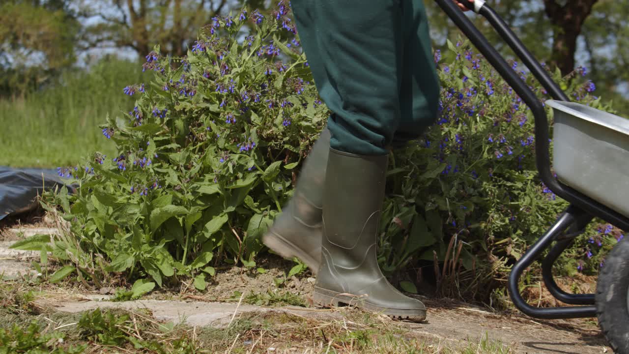 jardinero con botas de goma empujando una carretilla en el jardín
