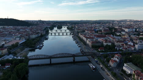 a drone view of prague during sunset - flying over the vltava river towards prague castle, train crossing the bridge