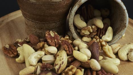 Two cups of assorted nuts rotate on wood board on black background
