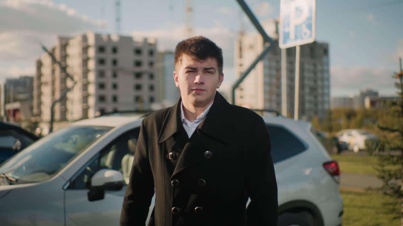 hombre de abrigo negro saliendo de su coche con una expresión seria en una vibrante zona urbana con coches estacionados, edificios modernos, vegetación, vehículos en movimiento y peatones