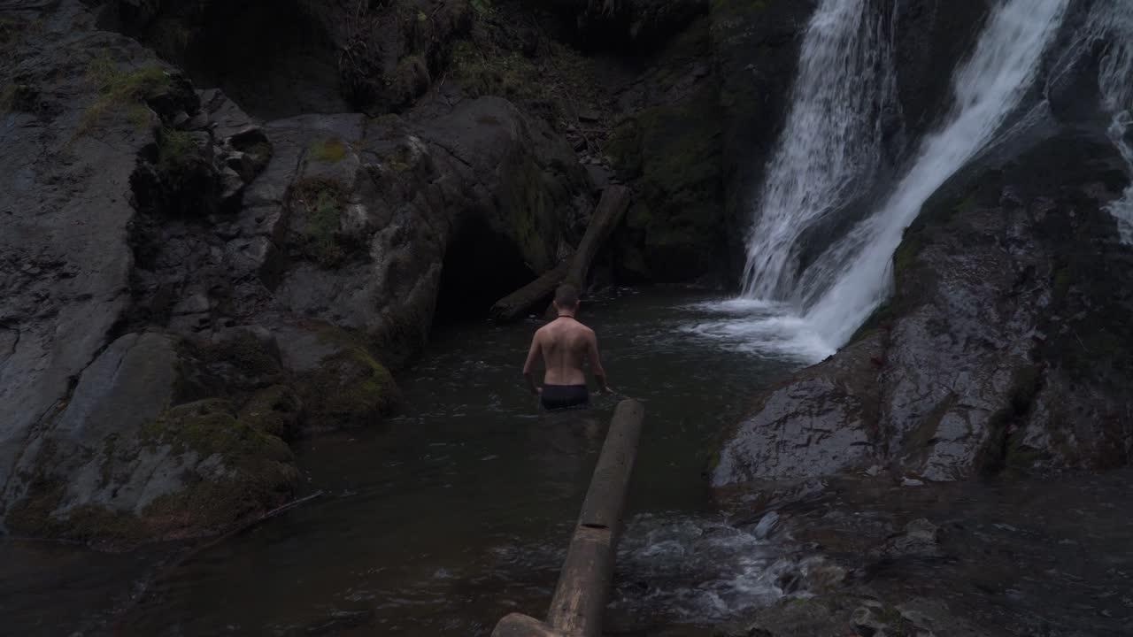 폭포에서 흐르는 물줄기를 따라 걷는 것을 즐기는 청년 - 중간 샷