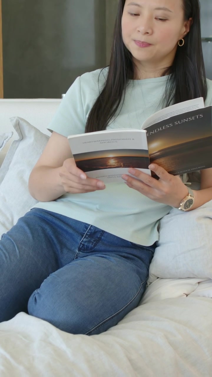 Vertical video: Reader in mint top hearing sound, glancing, paging ENDLESS SUNSETS on sofa to read