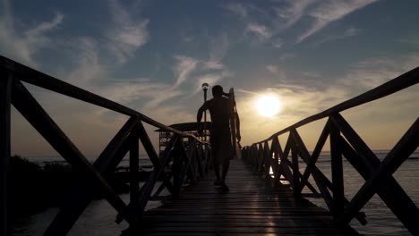 a fit surfer running down the pier at sunset hoping to catch one more wave, a slow motion tracking shot