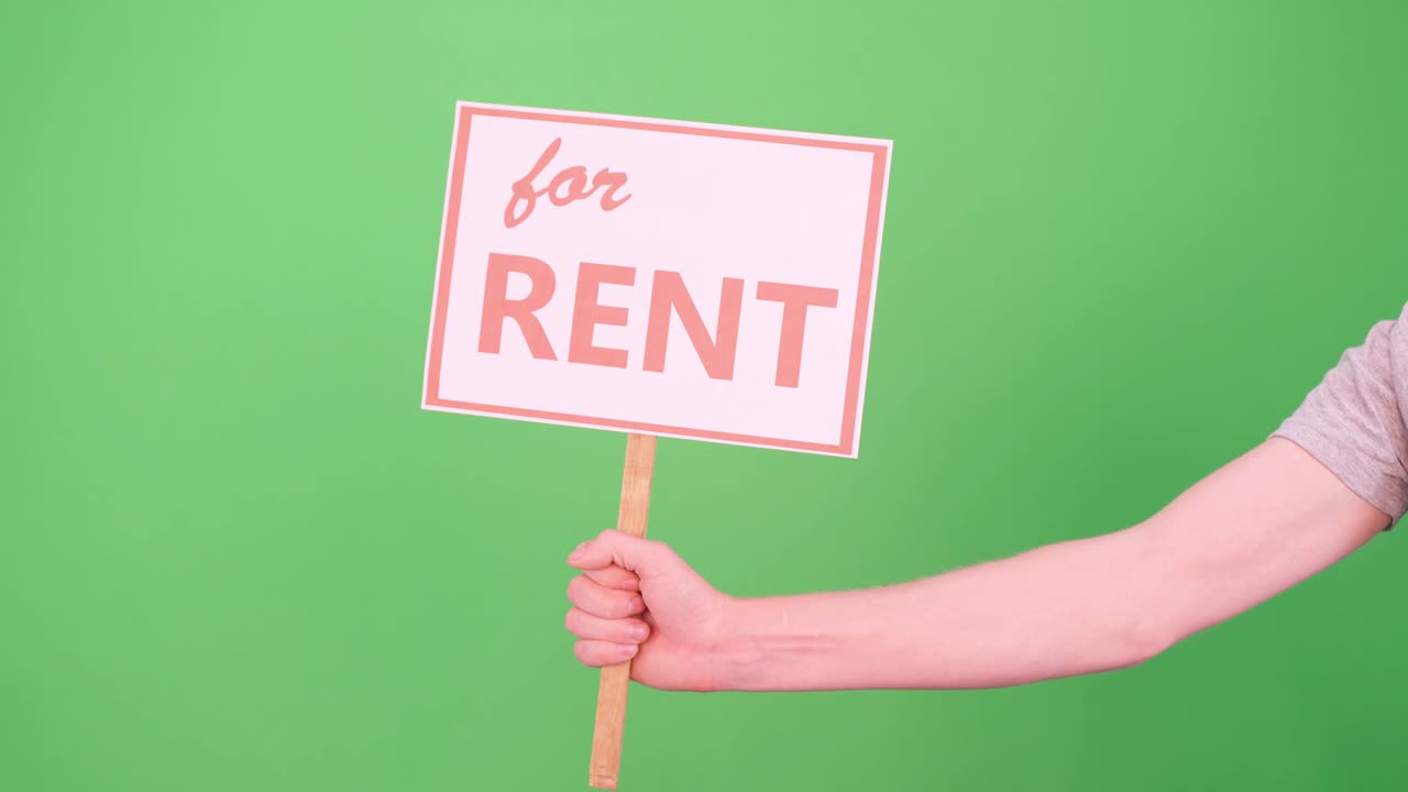 한 남자의 손은 초록색 배경의 크로마키에 임대료를 표시한 표지판을 올린다.