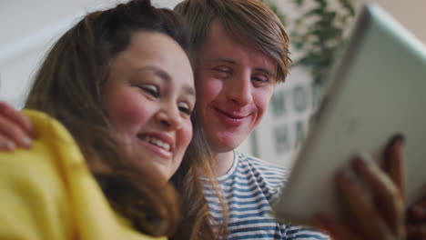 young downs syndrome couple sitting on sofa watching digital tablet at home