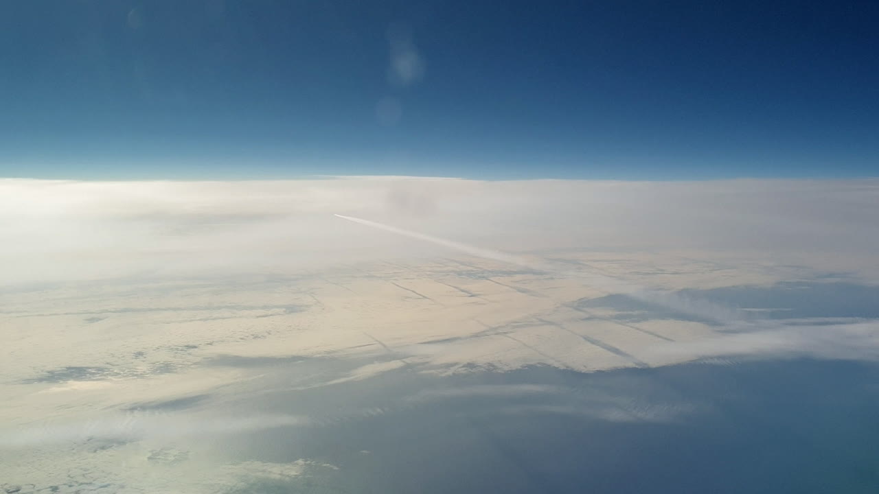 невероятный вид из кабины самолета, летящего высоко над облаками и оставляющего длинный белый конденсационный след в голубом небе