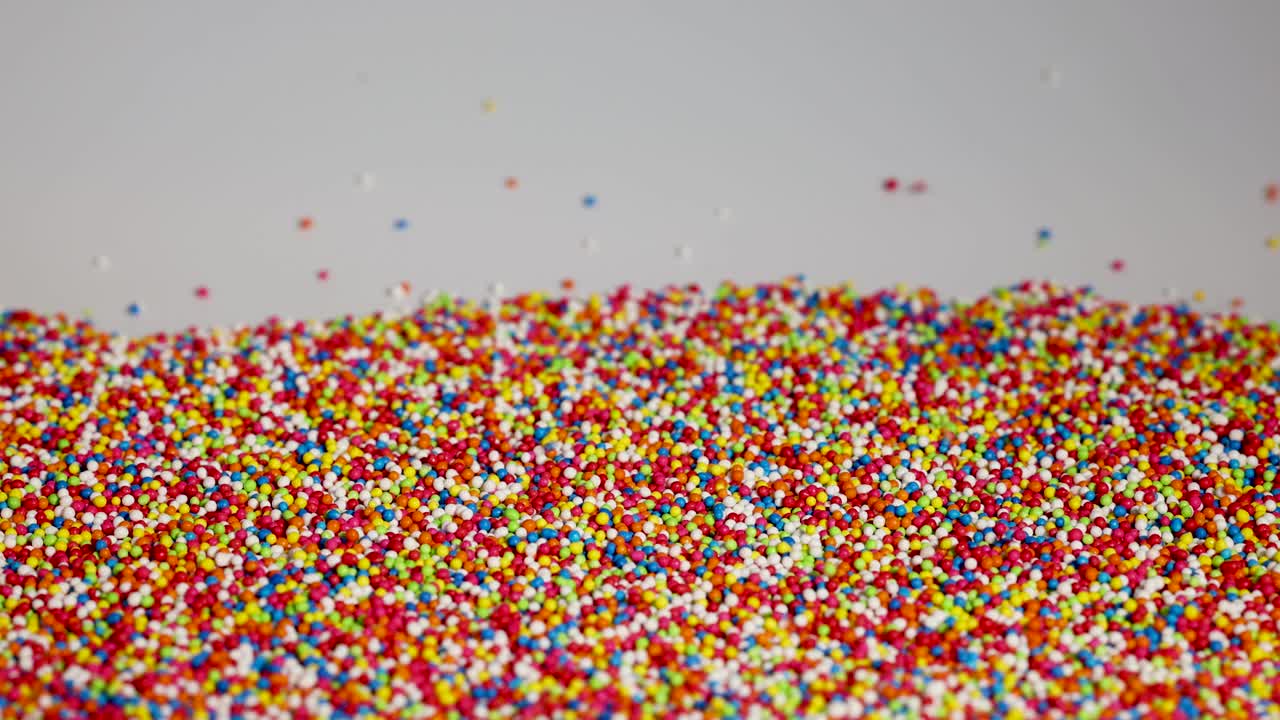 Vibrant sprinkles cascade onto a surface, creating a colorful, textured landscape against a neutral background