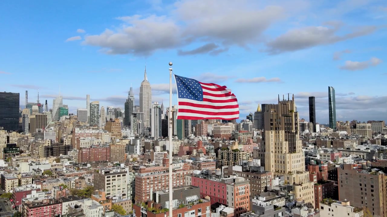 Filmový letecký záběr. Kroužení kolem americké vlajky ukazující silnou energii Manhattanu v pozadí.
