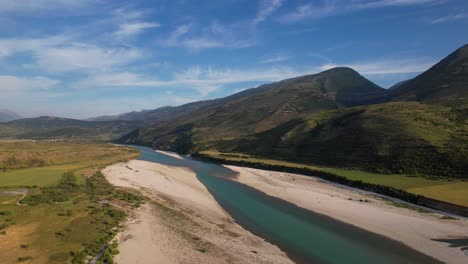 Emerald-river-Vjosa-in-Albania-streaming-into-valley-with-mountains-and-blue-sky-background