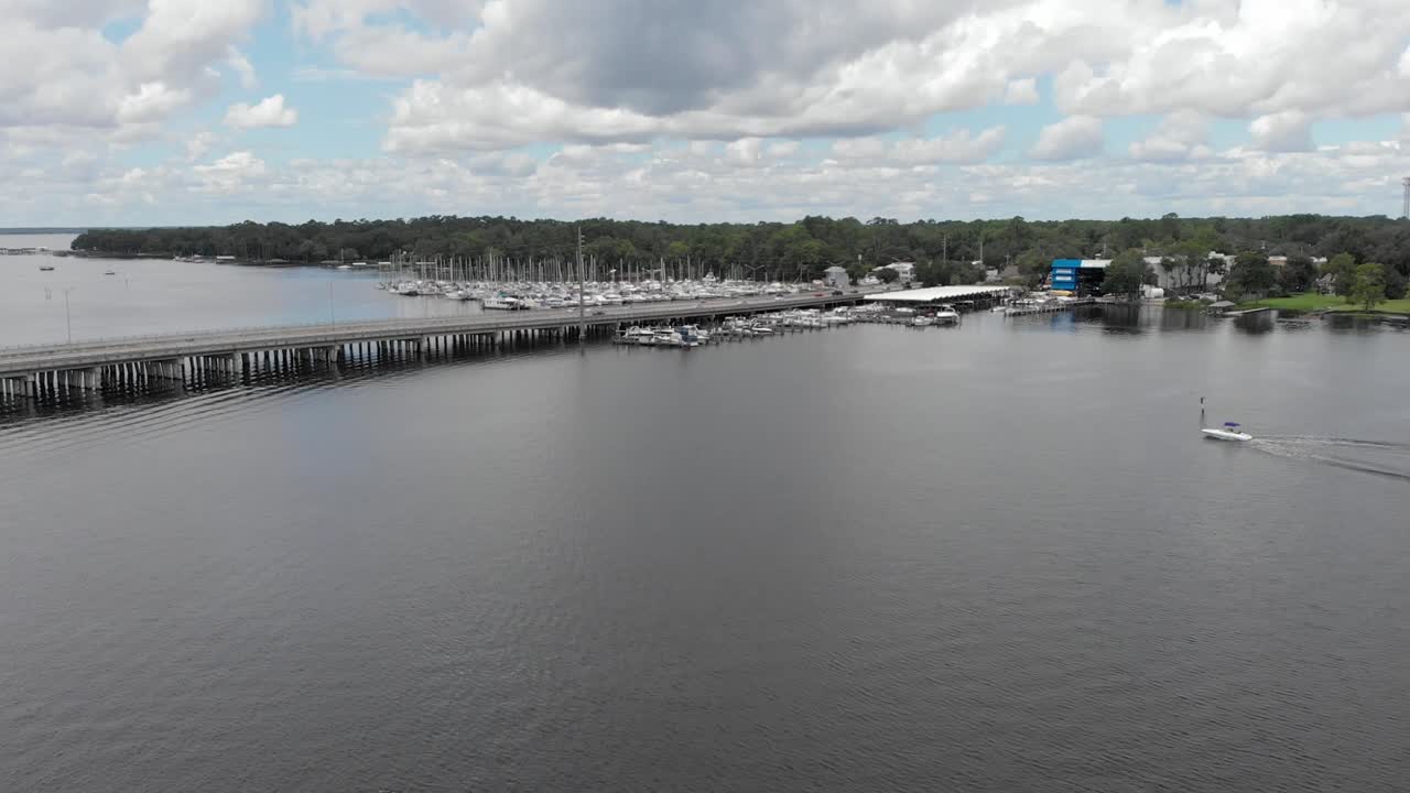 panorámica aérea disparada revelando la carretera y los barcos de agua carreteras coches que pasan por el cielo azul nubes blancas árboles en el lado de la carretera