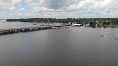 Aerial-pan-up-shot-revealing-the-highway-and-water-boats-roads-cars-passing-by-blue-sky-white-clouds-trees-in-on-side-of-highway