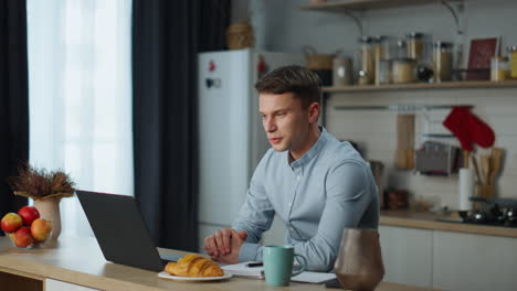 Worker-passing-online-interview-using-webcam-on-laptop-sitting-at-kitchen-table