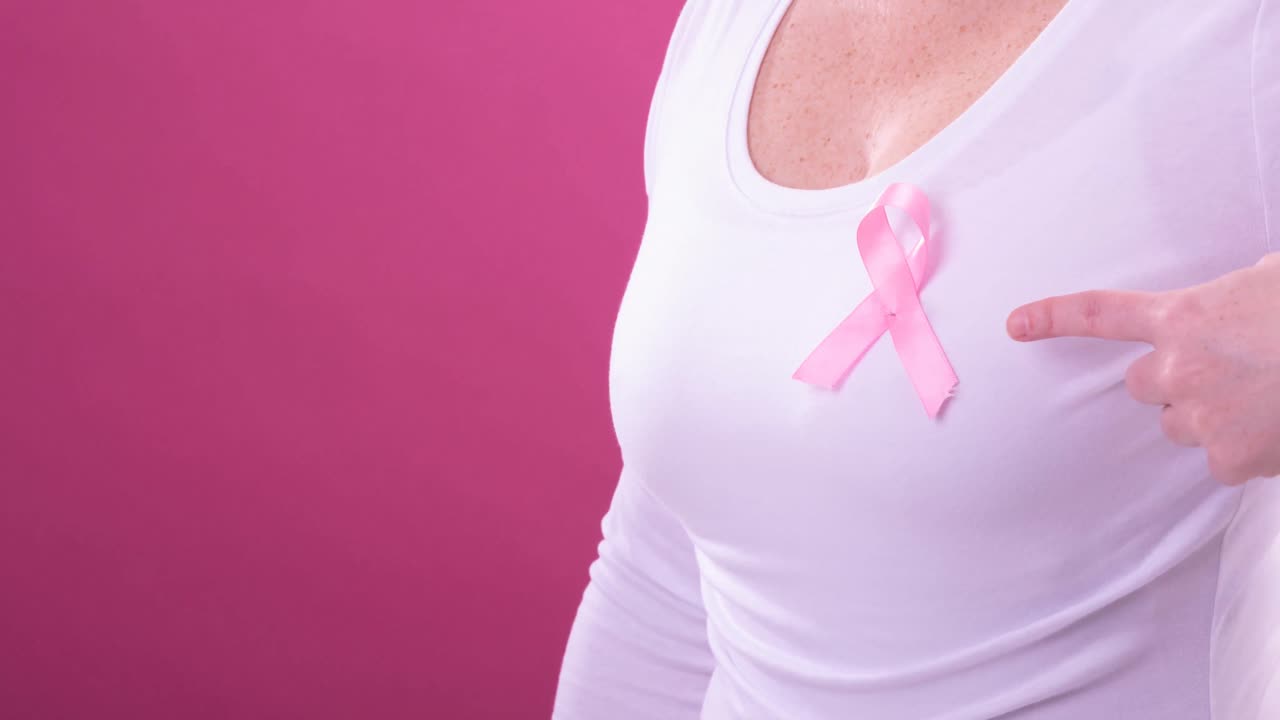 Video del mezzo busto di una donna caucasica che indossa un nastro rosa per la sensibilizzazione al cancro, con sfondo rosa.