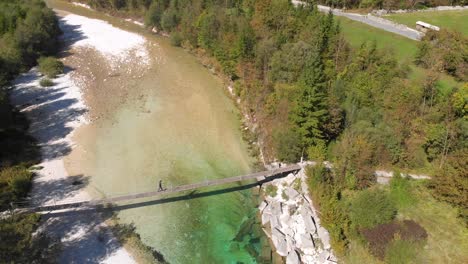 aerial side view of man walking across rope bridge over soca river in slovenia