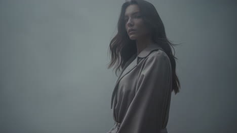woman in trench coat standing in fog