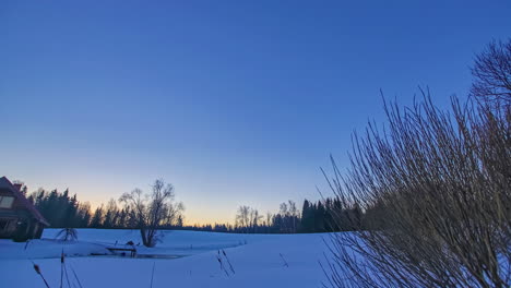 Tiro-De-Lapso-De-Tiempo-De-Hermoso-Amanecer-Sobre-Cabaña-De-Madera-A-Lo-Largo-Del-Cielo-Azul-Durante-El-Frío-Día-De-Invierno-Con-Campo-Cubierto-De-Nieve