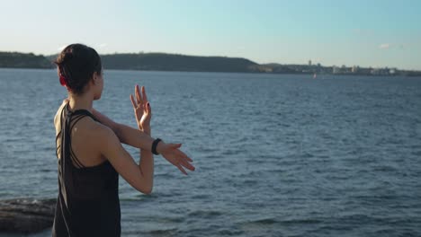 Young-female-stretches-her-arm-by-the-waters-edge-during-sunset