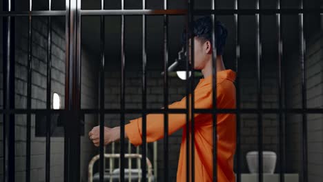 side view of asian male prisoner stretching out the hands surrender himself while standing in prison