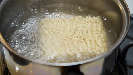 añadiendo un ladrillo de fideos ramen a una olla de agua hirviendo