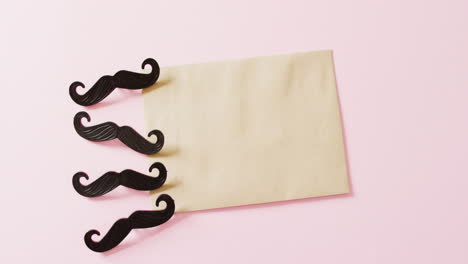 video de cuatro bigotes falsos negros y un sobre amarillo con espacio de copia en un fondo rosa