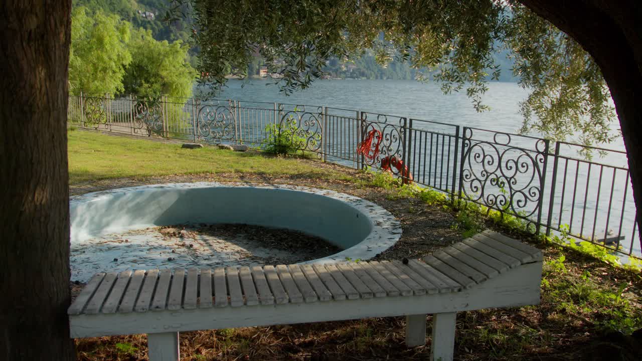 Calm static shot of empty pool and tree facing Lake Como, Italy (Lago di Como, Italia) with sparkling water at sunset