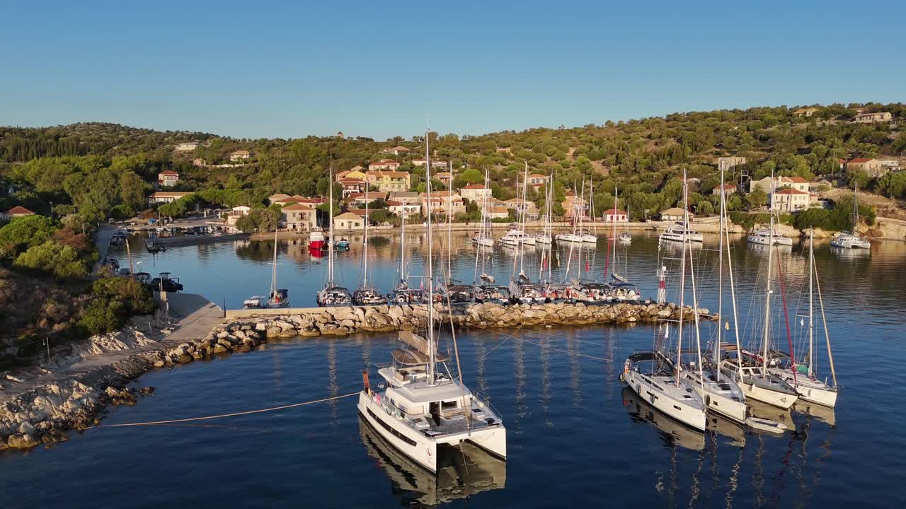 Kastos Island,aerial view pan right forward over harbor towards the open sea where sailboats anchored on a sunny day.Lot of boats at the town quay and outside on anchor.Beautiful green Greek Island