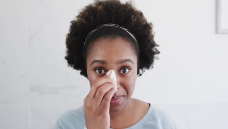 happy african american woman cleansing face with cotton pad, smiling in bathroom mirror, slow motion