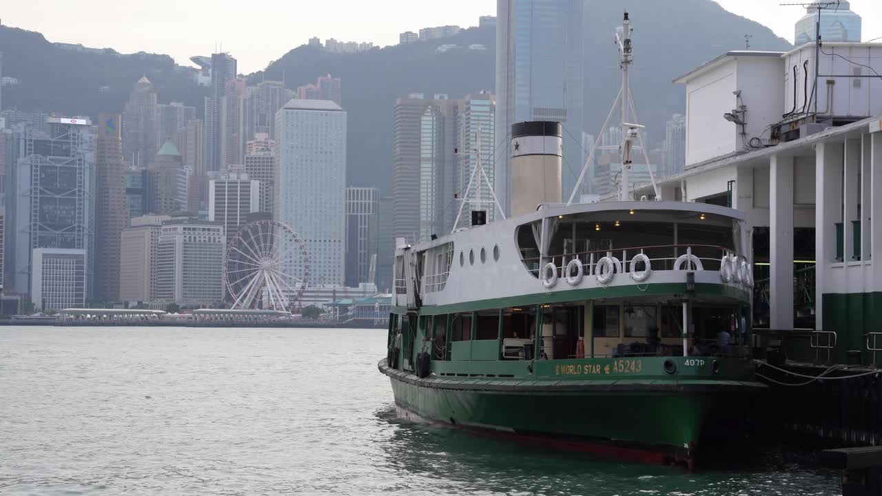 la terminal de ferry y un barco vacío con una vista de la rueda de observación de hong kong y los edificios del horizonte bajo un cielo gris y brumoso debido a la contaminación del aire, china