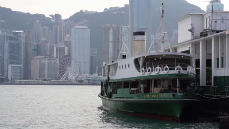 La-Terminal-Del-Ferry-Y-Un-Barco-Vacío-Con-Vistas-A-La-Noria-De-Observación-De-Hong-Kong-Y-A-Los-Edificios-Del-Horizonte-Bajo-Un-Cielo-Gris-Y-Brumoso-Debido-A-La-Contaminación-Del-Aire,-China