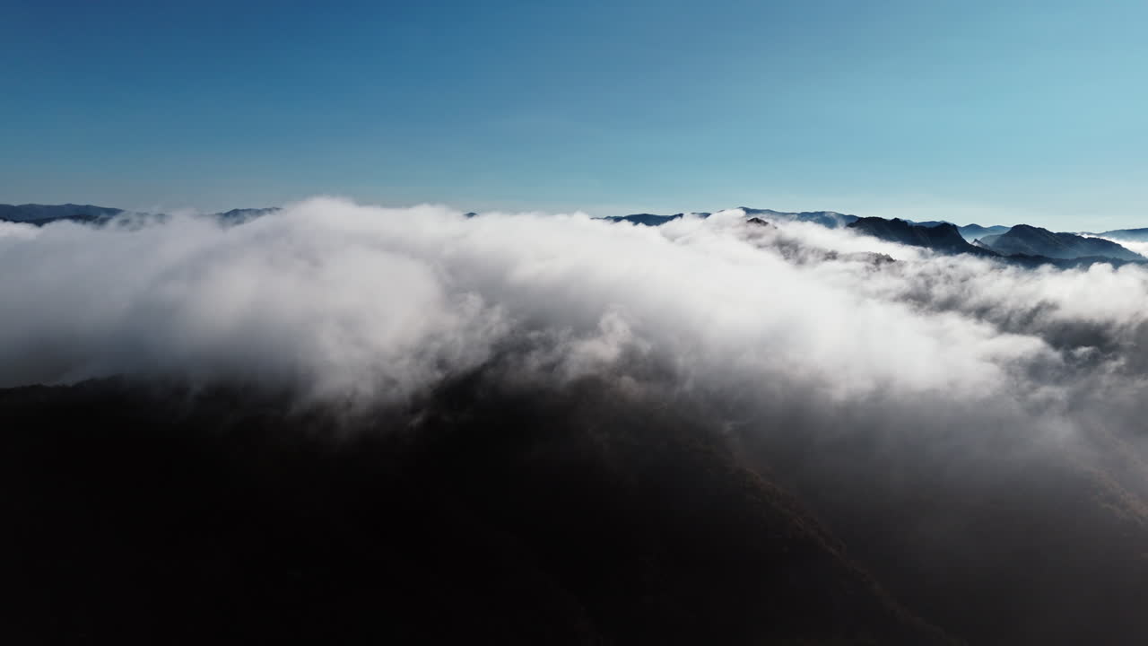 Tidligt om morgenen omfavner skyerne blidt bjergtoppene under en klar, blå himmel.