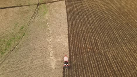 An-aerial-footage-revealing-an-orange-tractor-moving-up-the-frame,-tilling-a-farmland-in-Muak-Klek,-Saraburi,-Thailand