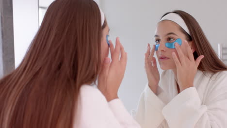 applying blue eye patches, woman looking in mirror during home spa routine