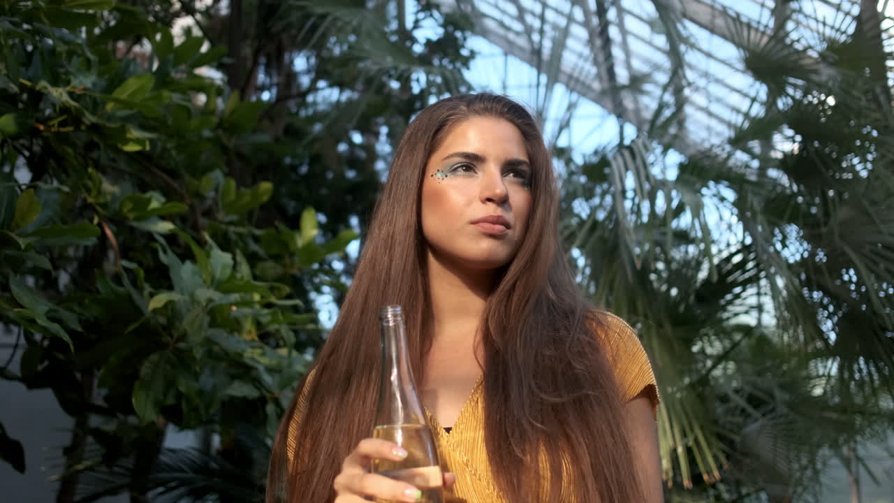 젊은 소녀 모델이 열대 온실에서 물을 마시고 있습니다.