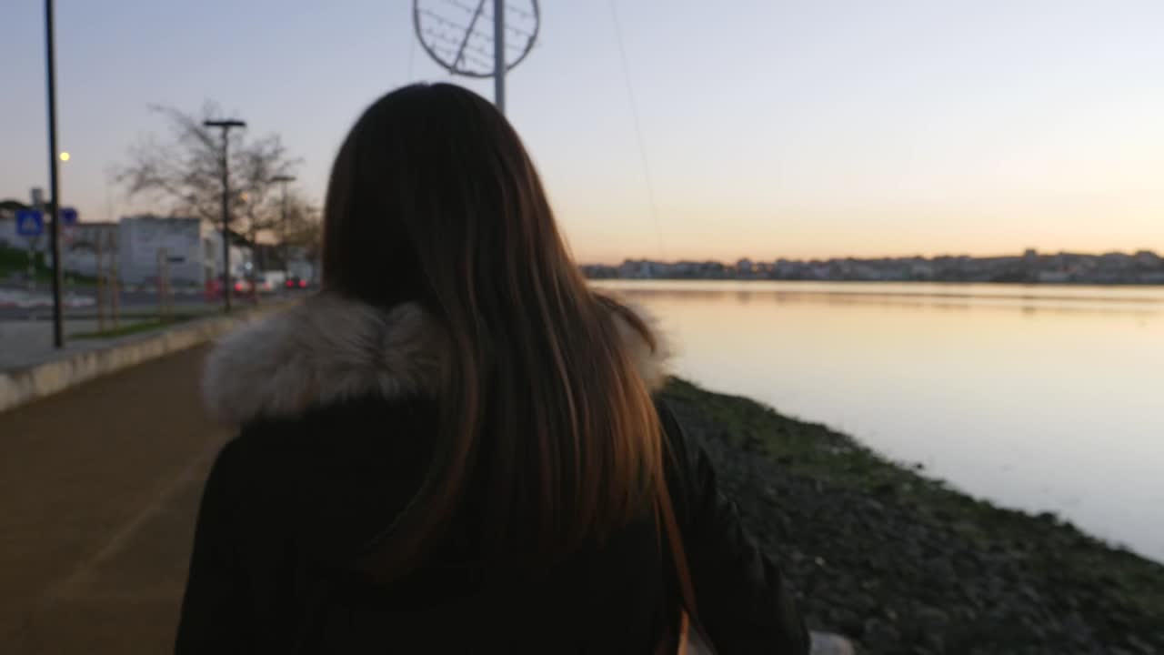Woman walking by the river at sunset