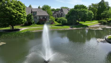 Drohnenansicht-Von-Stadthäusern-In-Einer-Parkähnlichen-Umgebung-Mit-Einem-Kleinen-See-Und-Einem-Brunnen