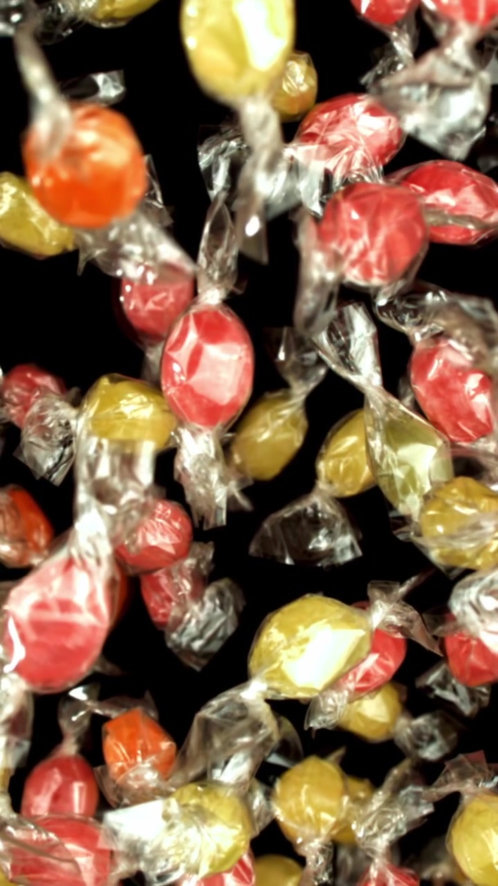Caramelle colorate incartate che cadono al rallentatore su sfondo nero