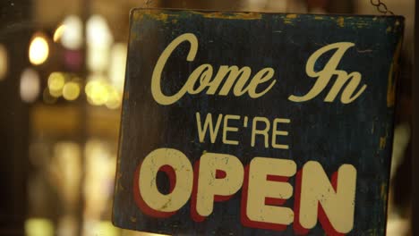 close-up of a vintage 'come in we're open' sign in a cozy cafe setting, inviting atmosphere