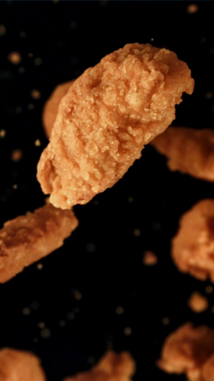 Nuggets de frango fritos crocantes flutuando em câmera lenta em fundo preto