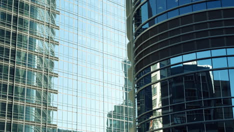 modern walls are made of glass and steel with reflections of buildings and blue sky