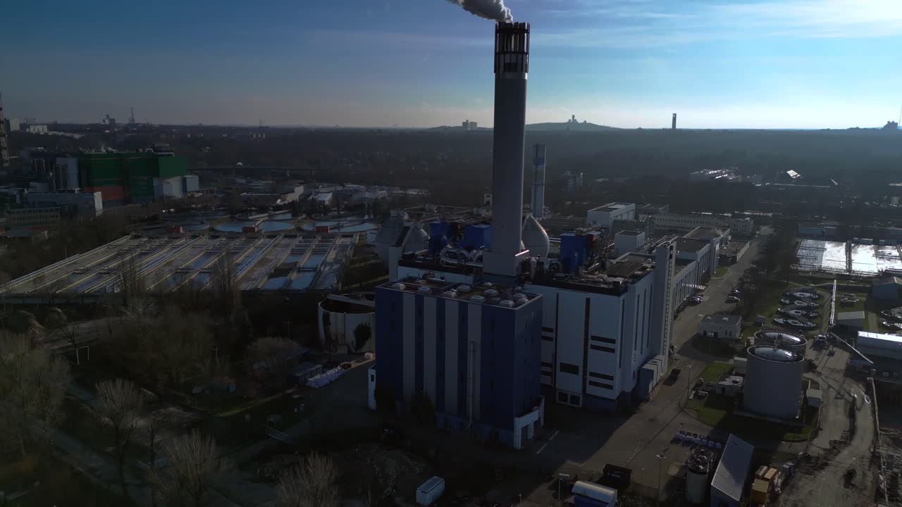 Waste to energy plant emitting smoke from its chimney, located near an urban area, environmental impact of waste. Nice aerial view flight tilt up drone
