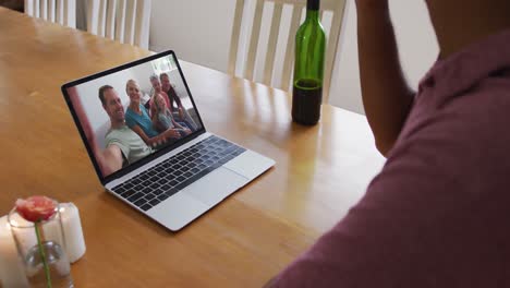 Mid-section-of-african-american-man-drinking-wine-while-having-a-video-call-on-laptop-at-home