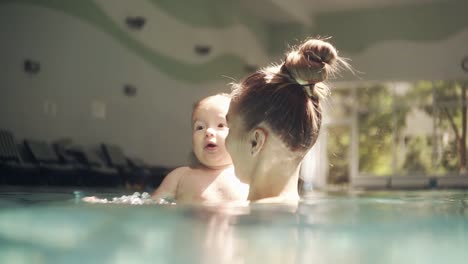 Glückliche-Junge-Mutter,-Die-Mit-Ihrem-Baby-Im-Pool-Spielt-Und-Das-Wasser-Spritzt