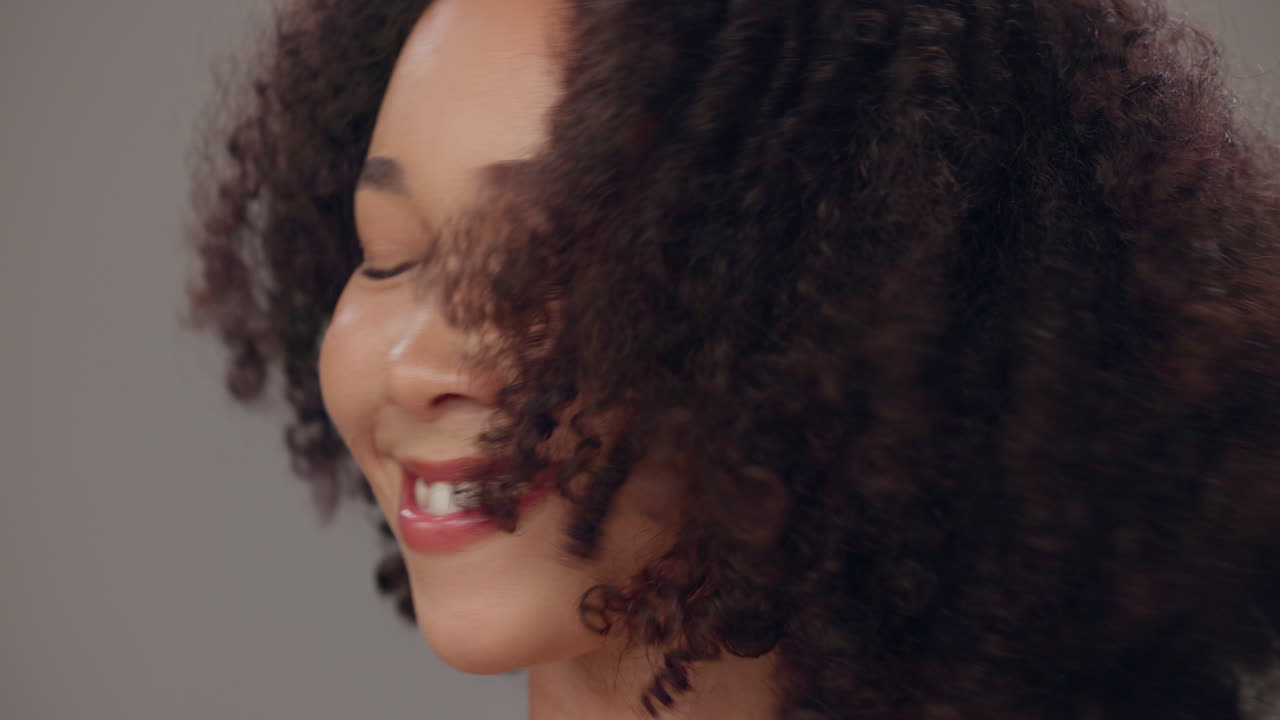 카메라를 향해 미소 짓는 곱슬 머리카락을 가진 행복한 젊은 여성