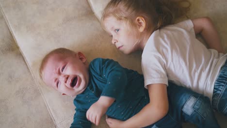 girl tries to calm little brother hugging baby on big bed