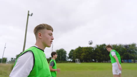 male soccer players training, warming up and throwing ball in pairs on pitch