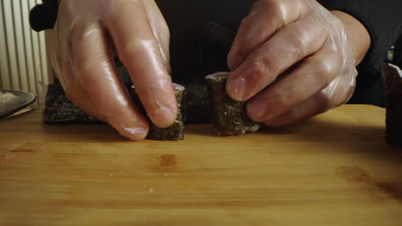 Close-up of hands preparing sushi rolls on a wooden board