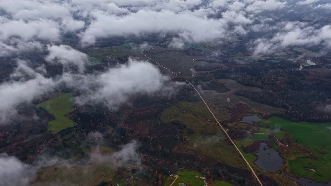 Statisk flyfoto av skyer som driver over skog og landevei