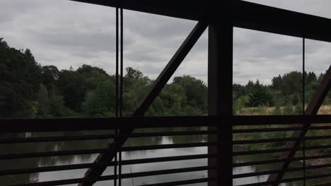 Looking-through-the-railing-on-a-rusty-footbridge-over-a-river-on-an-overcast-summer-day-in-Oregon