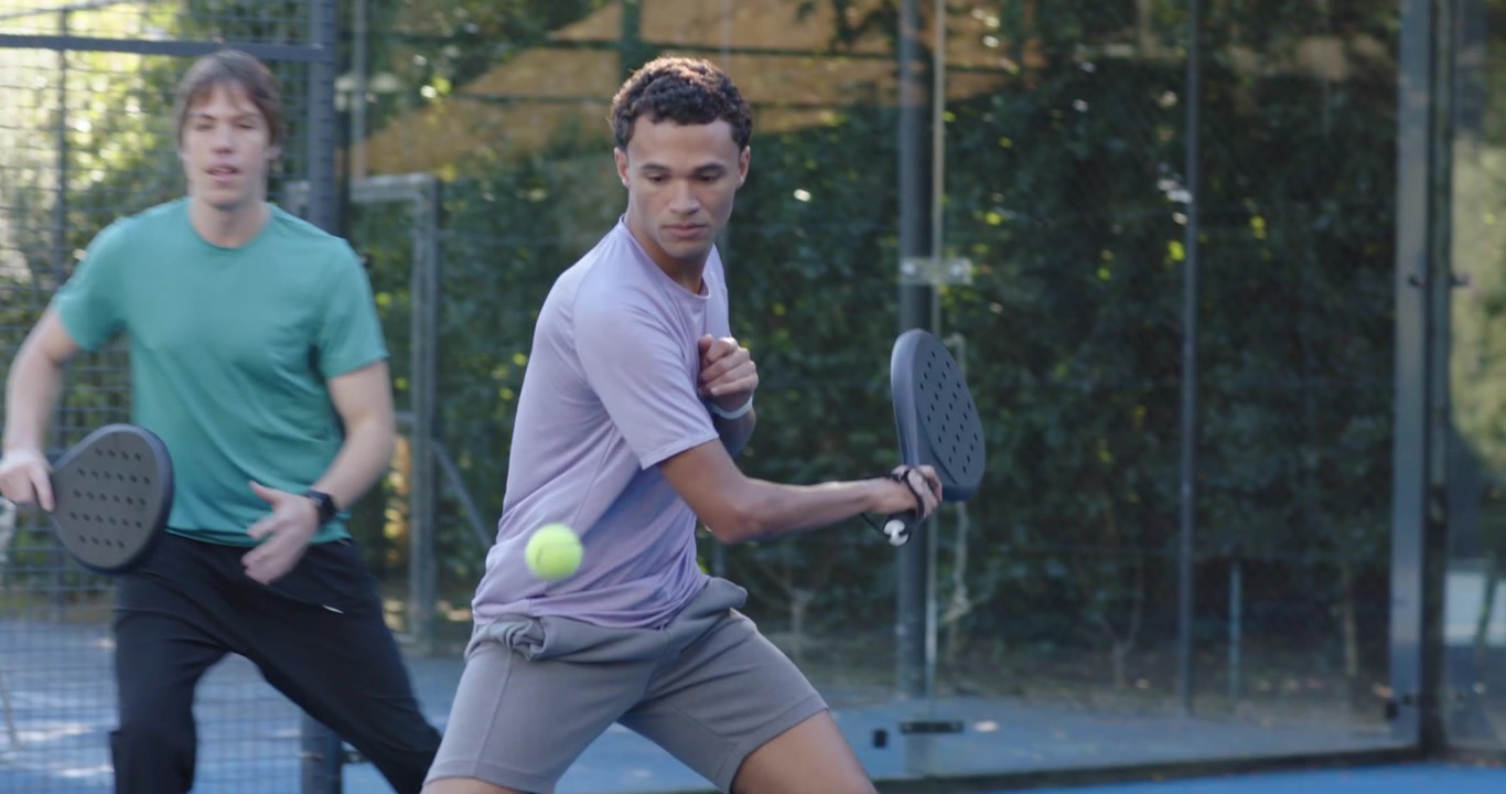 Diverse men lavender-shirted lunging returning incoming yellow ball with black paddle on blue court