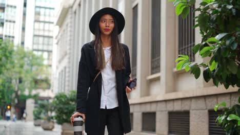 Hispanic-woman-with-takeaway-coffee-and-smartphone